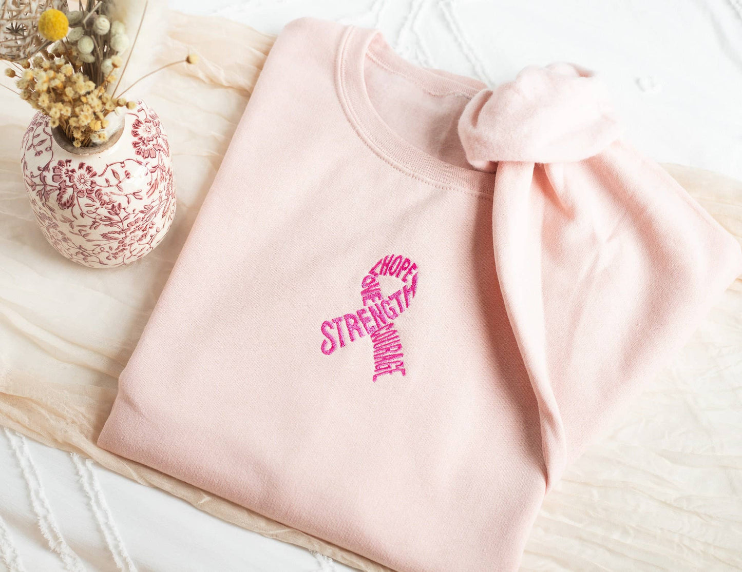 Pink sweatshirt with motivational text on a light wooden surface with a decorative vase.