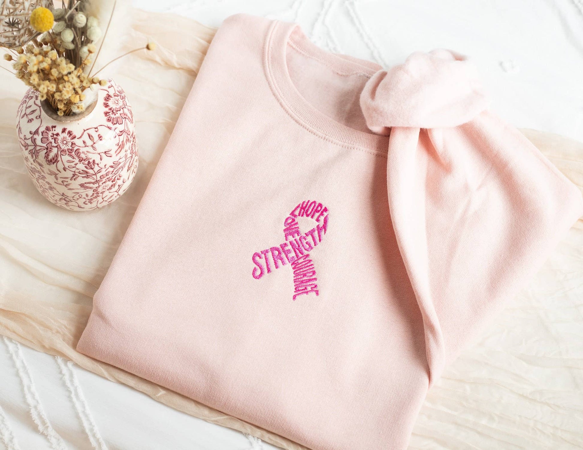 Pink sweatshirt with motivational text on a light wooden surface with a decorative vase.