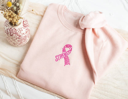 Pink sweatshirt with motivational text on a light wooden surface with a decorative vase.