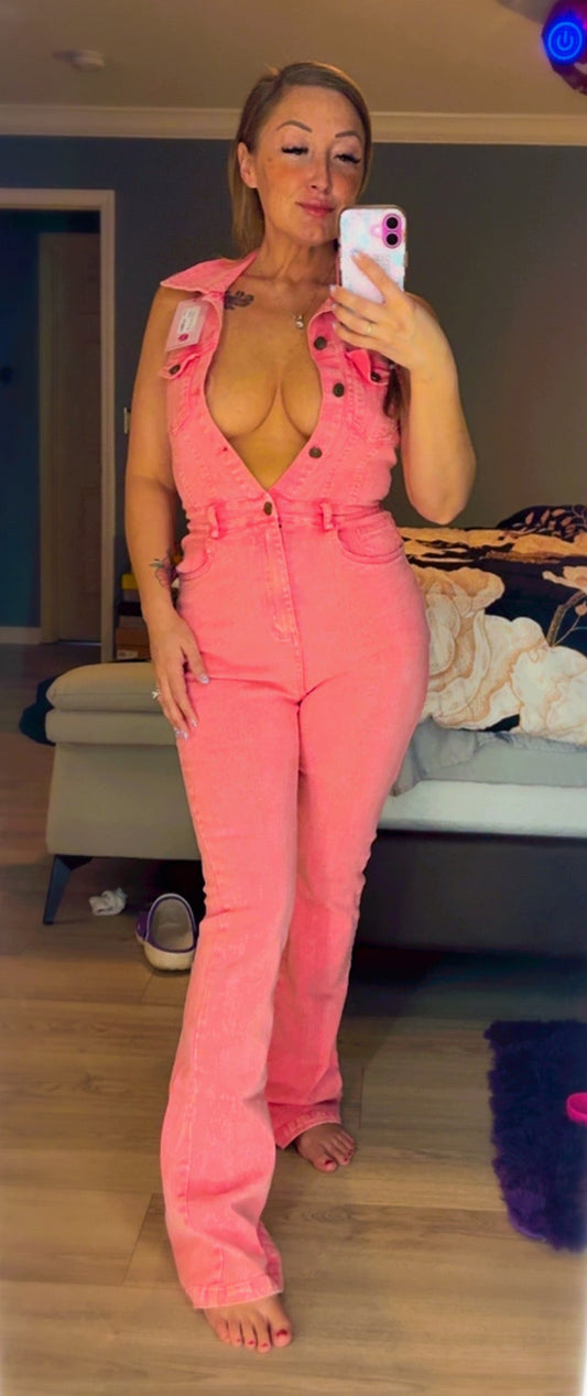 Person wearing a pink jumpsuit taking a mirror selfie in a room.